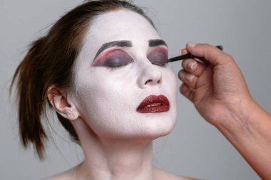 Beyaz tabanlı bir yüzün cesur, dramatik gözleri ve dudakları olan sanatsal bir makyaj uygulamasının yakın çekimi.