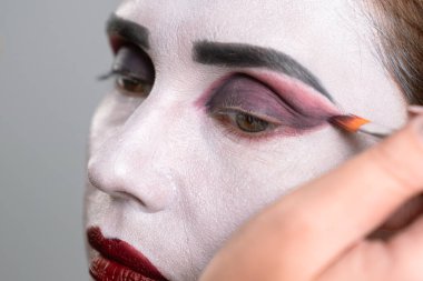 Sanatsal makyaj uygulamasının yakın çekimi beyaz tabanlı ve koyu renk gözlüklü fırçayı gösteriyor.