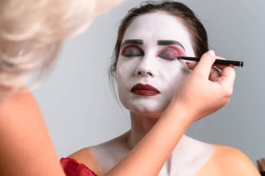 Bir makyaj sanatçısı dramatik sahne makyajını ustalıkla uygular, modellerin yüzlerini hassasiyet ve yaratıcılıkla değiştirir..