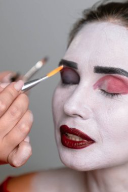Sanatsal yüz makyajını dramatik bir etki yaratmak için kalın renkler ve hassas fırça darbeleri kullanarak kapat.