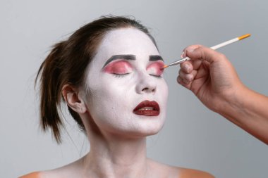 Bir modacı canlı pembe ve beyaz tonlarını kullanarak çarpıcı bir makyaj uygular, sanatsal ve benzersiz bir görünüm yaratır.