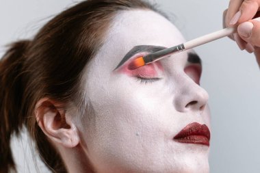 Makyaj sanatçısı bir modele renkli bir göz farı sürer, titiz fırça darbeleriyle canlı pembe tonlara odaklanır..