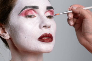 Yüzünde koyu kırmızı ve siyah aksanlı sanatsal makyaj uygulamasını gösteren yakın plan bir fotoğraf..