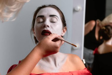 Yakından çekilen bir fotoğrafta beyaz boyalı bir yüze kırmızı dudak sürüp dramatik makyajı vurguluyor..