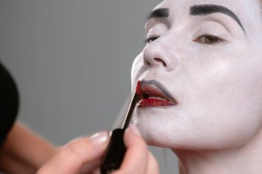 Yakından çekilen bir fotoğrafta beyaz boyalı bir yüze kırmızı dudak sürüp dramatik makyajı vurguluyor..