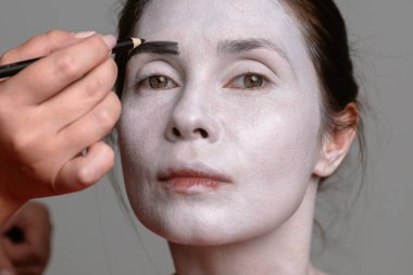 Yakından çekilen fotoğrafta siyah kaşlarını beyaza boyayan bir insan yüzü görülüyor. Dramatik makyajı vurguluyor..