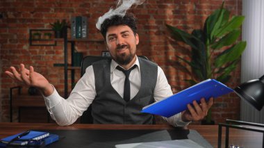 Yelek ve kravat takmış özgüvenli, sakallı bir iş adamı masasında otururken mavi bir klasör tutar. Tuğla bir duvar ve arka planda bitkilerle profesyonellik ve sakinlik yayar..