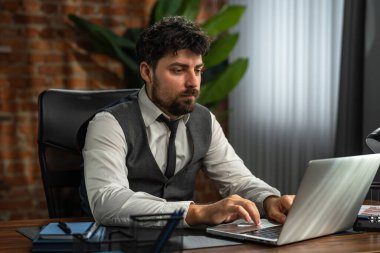 Odaklanmış bir iş adamı, modern ofis ortamında özenle dizüstü bilgisayarı üzerinde çalışır, verimlilik ve konsantrasyon gösterir..