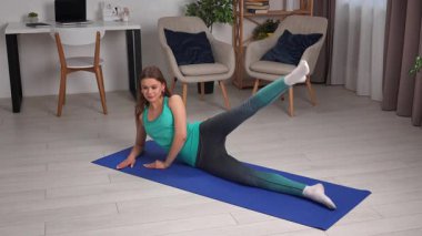 Genç bir kadın, içeride mavi bir minder üzerinde yoga egzersizleri yapıyor, esneklik ve gevşemeye odaklanıyor..