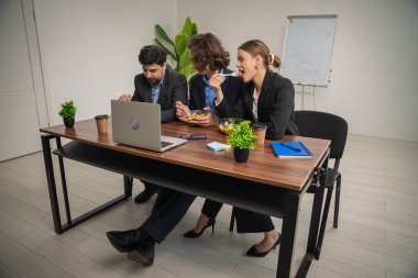 Üç meslektaştan oluşan bir grup, modern ofis ortamında öğle yemeği molası verirken bir tartışma içerisindeler..