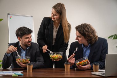 Bir grup profesyonel iş adamı ofis ortamında sağlıklı bir öğle yemeğinin tadını çıkarıyor ve takım çalışmasını destekliyor..