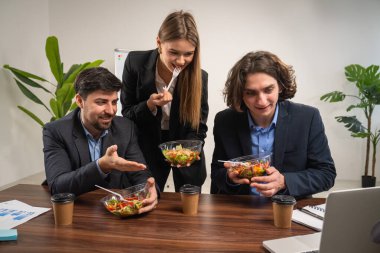 Modern bir ofiste üç meslektaş sağlıklı bir salatanın tadını çıkarırken canlı bir sohbet yapıyorlar..