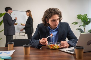 Bir ofis çalışanı laptoptaki verileri incelerken sağlıklı bir salatadan zevk alır, çoklu görev becerilerini vurgular.