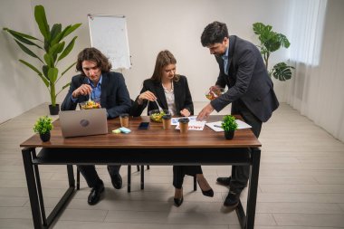 Meslektaşlar masa etrafında tartışıyorlar, fikirleri paylaşıyorlar ve ofis toplantısı sırasında öğle yemeği yiyorlar..