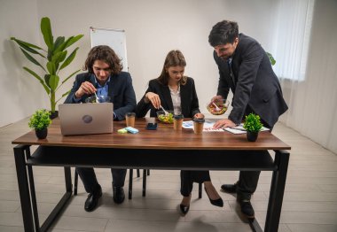Üç meslektaş öğle yemeğinin tadını çıkarırken toplantı yapıyorlar. Bir adam çizelgesini gösterir ve bir şeyi açıklar..