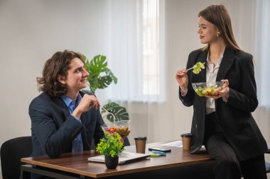 İki iş adamı öğle yemeği molası verir. Modern ofis ortamında salata ve kahvenin tadını çıkarırlar..