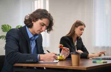 İki profesyonel masalarındaki işe odaklanırken, biri yazı yazarken diğeri dizüstü bilgisayar kullanıyor. Kahve ve salata hazır..