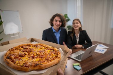 Modern bir ofisteki iki meslektaş lezzetli bir pizza ziyafetinin tadını çıkarmak için ara verir. Kapat.