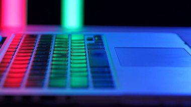 Canlı neon ışıkları altında bir dizüstü bilgisayar klavyesi, karanlık bir ortamda renkli tuşları vurguluyor.