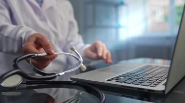 Modern sağlık teknolojisini sembolize eden steteskop tutarken dizüstü bilgisayar kullanan bir tıp uzmanı..
