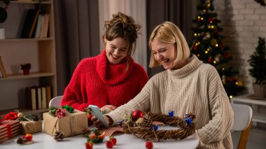İki kadın Noel için hazırlanırken şenlik ruhunun tadını çıkarıyorlar. Ev yapımı hediyeleri paketleyip telefonlarına görüntülü konuşma yapıyorlar..