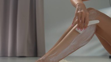 Bir kadın bacağına saç kesme kremi sürerek evde kendine iyi baktığını gösterir..