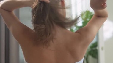 Bir kadın evde, güzellik rutinine odaklanmış, saçını dikkatlice örüyor. Sahne, iç düzende kişisel bakım ve güzellik ayinlerini yakalıyor..