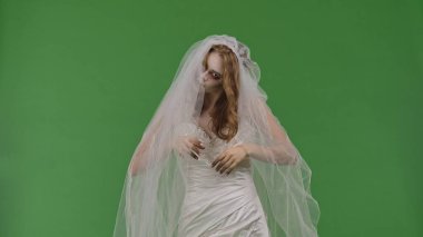 A woman dressed as a dead bride, in a white wedding dress and veil, stares fearfully into the camera. The ghostly bride stands against a green chroma key backdrop for Halloween or spooky projects.
