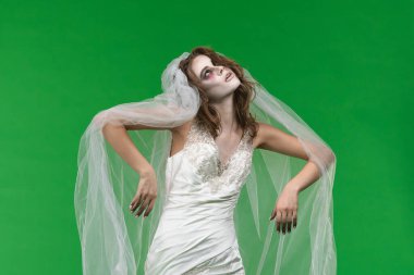 A woman dressed as a dead bride, in a white wedding dress and veil, moves terribly like a zombie. The ghostly bride stands against a green chroma key backdrop for Halloween or spooky projects.