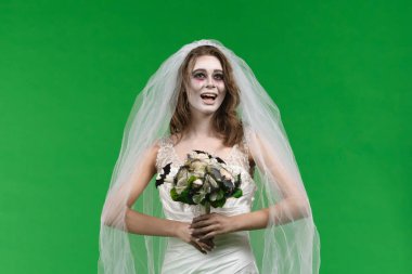 A woman dressed as a dead bride, wearing a white wedding dress and veil, looks at the camera and smiles. The ghostly bride stands against a green chroma key backdrop for Halloween or spooky projects.