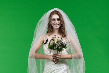A woman dressed as a dead bride, wearing a white wedding dress and veil, looks at the camera and smiles. The ghostly bride stands against a green chroma key backdrop for Halloween or spooky projects.