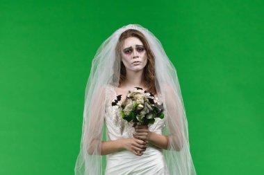 A woman dressed as a dead bride, in a white wedding dress and veil, looks sadly into the camera. The ghostly bride stands against a green chroma key backdrop for Halloween or spooky projects.