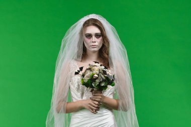 A woman dressed as a dead bride, in a white wedding dress and veil, looks sadly into the camera. The ghostly bride stands against a green chroma key backdrop for Halloween or spooky projects.