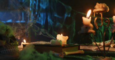 Eerie Halloween setting featuring skull, candles, and old books on a table, surrounded by spider webs.