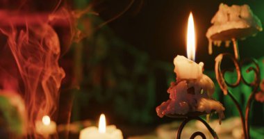Eerie Halloween scene featuring candles with melting wax, surrounded by mysterious smoke and colorful light.