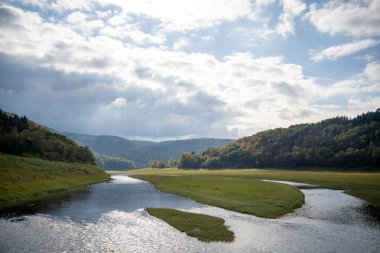 Geniş açılı bir manzara, yemyeşil bir vadiden akan dolambaçlı bir nehri yakalar. Çimenli adaların ve alçak kıyıların etrafındaki su, huzurlu ve sakin bir manzara yaratıyor. Nehir yuvarlanan tepelerle çevrili..