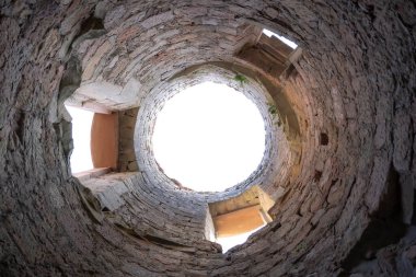 Dramatik ve benzersiz bir alçak açı, yüksek bir taş yapının tabanından geniş mercek görüntüsü, muhtemelen antik bir kale kulesi ya da kuyu. Kaba, dokulu taş duvarlar yukarıya doğru kıvrılır, yukarıdaki parlak dairesel açıklığa doğru gözleri çeker..