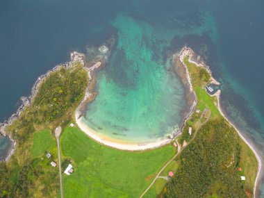 Bu büyüleyici dikey hava fotoğrafıyla tenha bir sahil koyunun güzelliğini keşfedin. El değmemiş, at nalı şeklinde beyaz kumlu bir sahil kristal berraklığında turkuaz bir su havuzu kaplar ve kumlu deniz tabanını ortaya çıkarır..