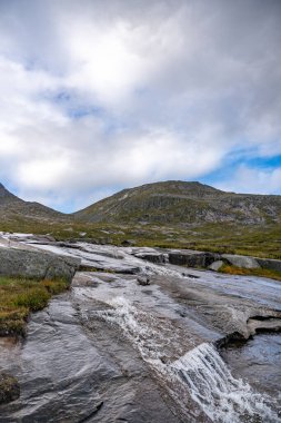 Geniş, pürüzsüz kaya oluşumları üzerinde akan ve büyüleyici beyaz köpük desenleri oluşturan bir dizi canlı su şelalesinin yer aldığı güzel bir açık hava çekimi. Islak, koyu gri ve kahverengi kayalar canlı hareketle tezat oluşturuyor..