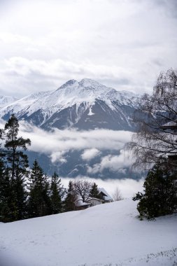 Kendinizi bu büyüleyici görüntüyle bir Alp kışının nefes kesici ihtişamına daldırın. Görkemli, karla kaplı bir dağ zirvesi ufka hakim olurken, sisli ya da bulutlu sakin bir tabaka orta zeminde sürükleniyor..