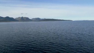 Büyüleyici bir sinematik çekim, Lofoten Adaları 'nın ikonik sivri dağlarını bir fiyordun sakin sularında yükselterek gösteriyor..