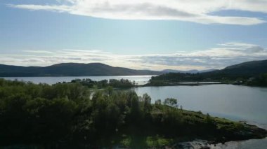 Huzurlu ve güneşli bir Norveç fiyordunun çekimleri. Huzurlu bir sahil köyü ve bulutlu, parlak mavi gökyüzünün altında yemyeşil dağlar..