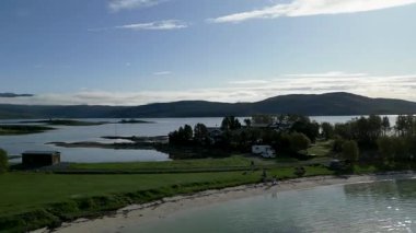 Sakin sular ve güneşli bir günde muhteşem bir dağ zeminiyle çevrili fiyorttaki pitoresk bir sahil köyünün çarpıcı yükseliş manzarası..