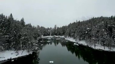 Huzurlu bir kış gölünden karla kaplı bir dağ köyü ve görkemli dağların panoramik manzarasına doğru pürüzsüz bir drone hareketi..