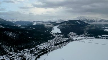 Alplerdeki karlı bir dağ köyünün insansız hava aracı görüntüsü. Çevresindeki tepelerin nefes kesici manzarası ve karla kaplı geniş bir manzarası var..
