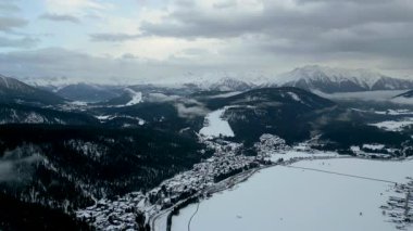 Karla kaplı bir dağ vadisinde, dramatik bir gökyüzünün altında kısmen donmuş bir gölü olan bir köyün çarpıcı hava manzarası..