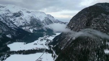 Karla kaplı bir köyü ve yükselen tepeler arasında kıvrılan bir nehri olan görkemli bir kış dağı vadisinde nefes kesici bir manzara..