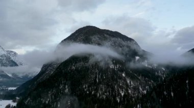 Doğal bulut ve sis hareketiyle kışın görkemli bir dağın çarpıcı uzak çekimi dramatik ve sakin bir atmosfer ekler..