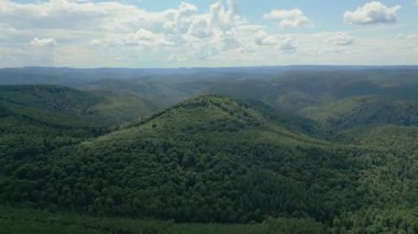 Görkemli bir dağ manzarasının durağan bir görüntüsü. Parlak, bulutlu bir gökyüzünün altında yoğun bir ormanla kaplı sonsuz yeşil tepeler ve vadiler..