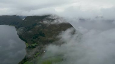 Huysuz bir fiyort manzarasının büyüleyici bir hava aracı görüntüsü. Engebeli yeşil dağlar ve Norveç 'te dramatik alçak asılı bulutlar ve sis..